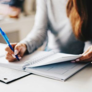 A white woman who is sitting in a classroom taking notes. Her face isn't showing.
