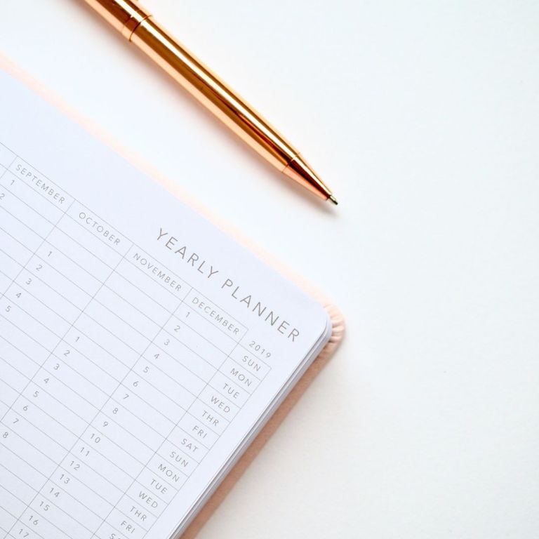 A ink pen and yearly planner is open on a table.