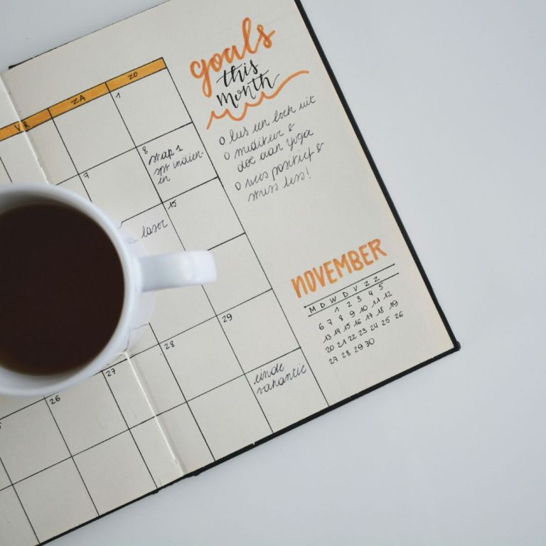 a planner with different entries within it and a coffee cup on top of it