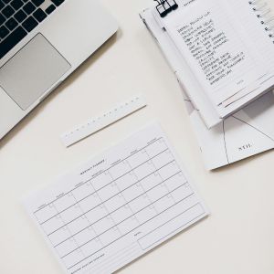 A white table with a grey laptop, a black calendar and a checklist on it.