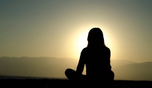 a woman meditating before a sunset