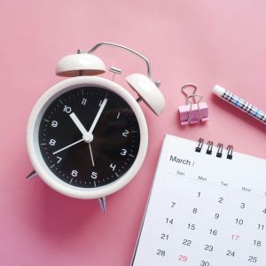 An alarm clock and calendar over a pink background.