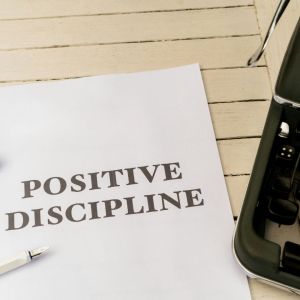 A piece of paper with a large title that says, "Positive Discipline" is on an outside table next to a green typewriter.