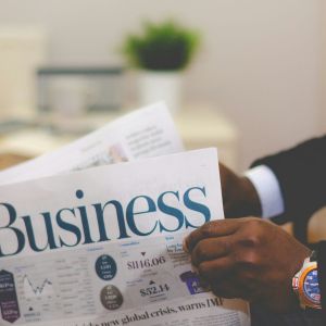 An African American reading the business section of a newspaper. He is wearing a suit with a gold and blue watch.