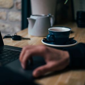 A man in his home office on the computer with a tea pot and cup on his desk.