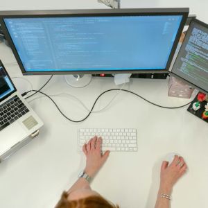 A woman in her office using 3 computers.