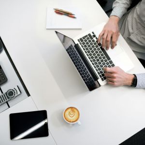 A man at a laptop with paper and two colored ink pens.